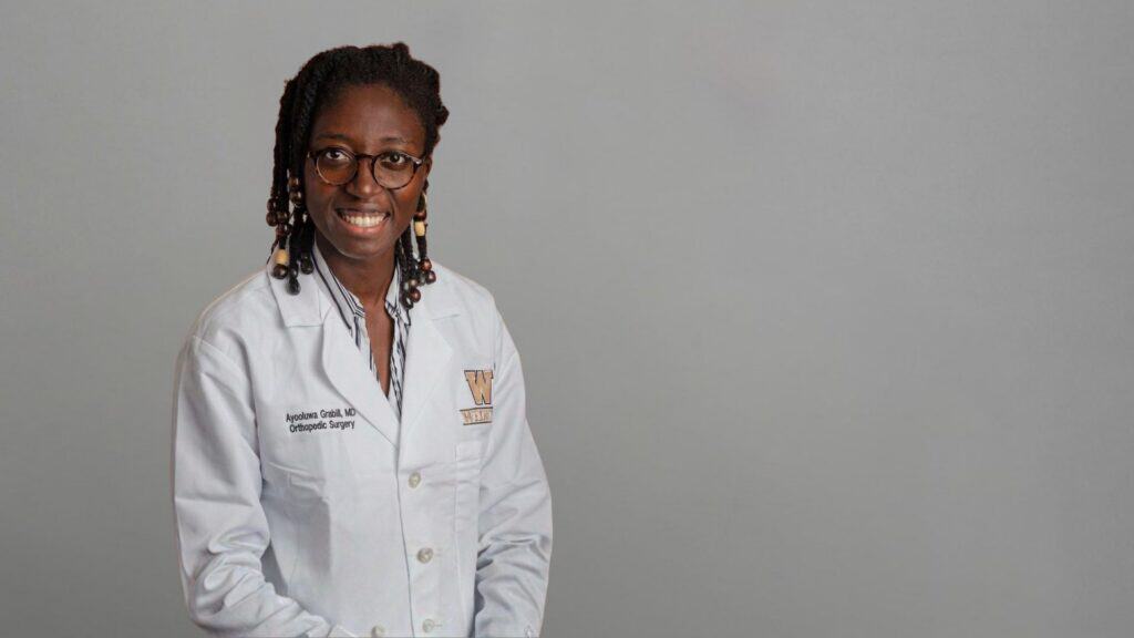 Dental professional wearing white coat and glasses smiling at camera.